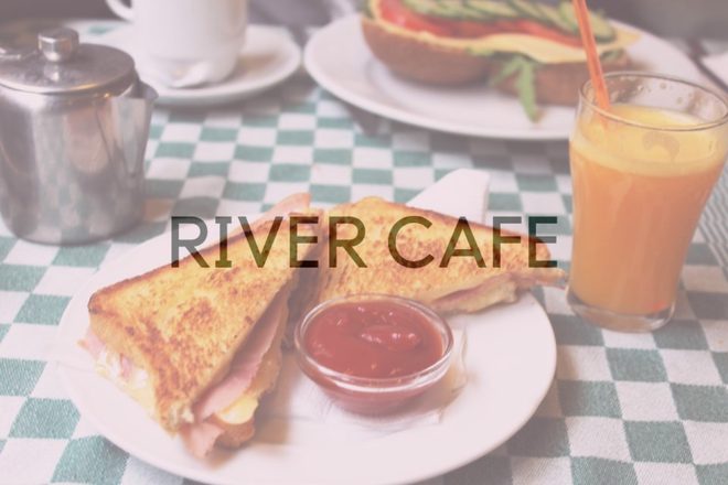 A toasted ham sandwich with a dip pot and a glass of orange juice on a checked tablecloth