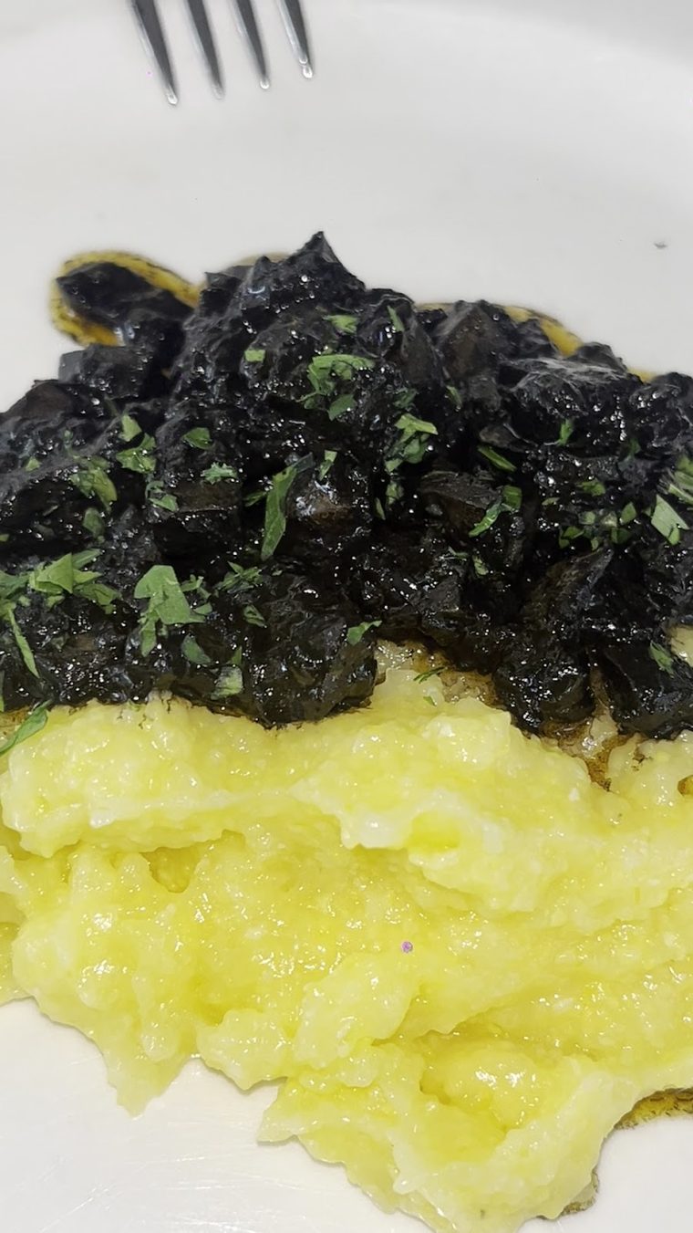 A close-up of a dark braised dish over yellow polenta